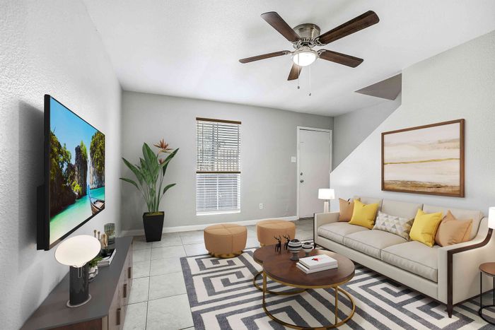 Modern living room featuring a cozy beige sofa with vibrant yellow cushions, elegant decor, and a sleek ceiling fan. A stylish flat-screen TV and beautiful indoor plant add charm to the bright, inviting space.