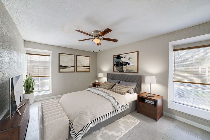 Modern bedroom with a cozy bed, stylish decor, large windows, and a ceiling fan, offering a bright and comfortable retreat.