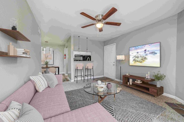 Chic living room with a stylish pink sofa, elegant ceiling fan, and a modern open-plan layout leading to a sleek kitchen.