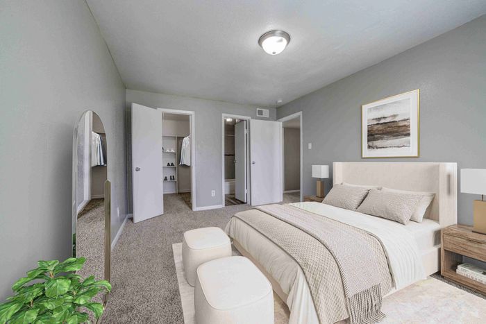 Elegant bedroom with plush carpet, modern decor, and a spacious walk-in closet. Bright and inviting atmosphere with fresh greenery accents.
