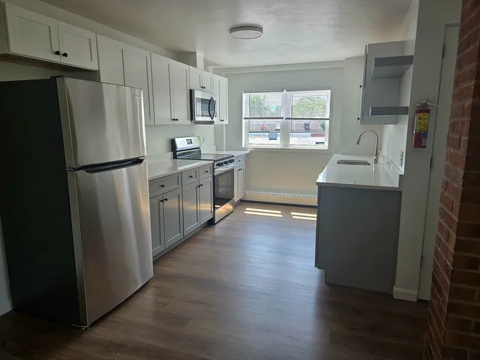 Bright and modern kitchen with stainless steel appliances, sleek white cabinets, and a large window with natural light.