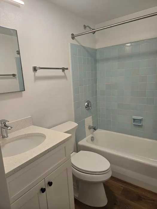 Bright and inviting bathroom featuring modern fixtures, a bathtub with elegant blue tile accents, and a sleek vanity with ample storage.