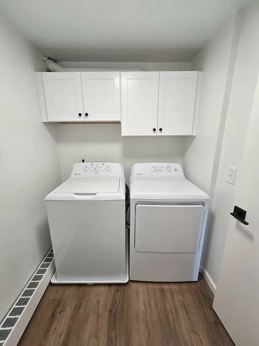 Modern laundry room with spacious washer and dryer, complemented by sleek white cabinetry and elegant wood flooring.
