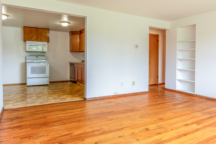 Bright and inviting open-concept space featuring a cozy kitchen with modern appliances, sleek hardwood floors, and built-in shelving for optimal storage.