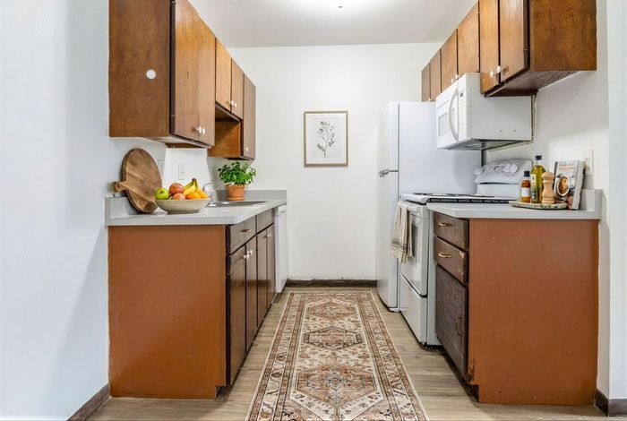 Charming galley kitchen featuring warm wooden cabinets, sleek countertops, a cozy runner rug, and modern appliances for a stylish culinary space.