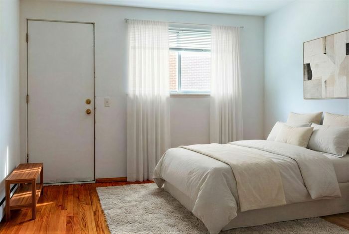 Bright and airy bedroom with soft natural light, featuring modern white decor and elegant hardwood flooring.