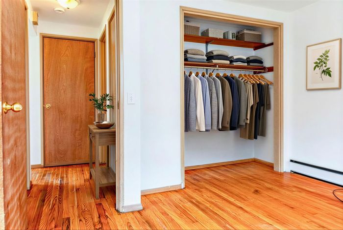 Inviting walk-in closet with neatly organized clothing and warm wooden floors, leading to a cozy wooden door hallway.