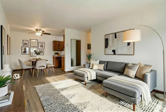 Bright, modern living area featuring a stylish gray sectional sofa, chic dining set, and contemporary decor with elegant wooden flooring.