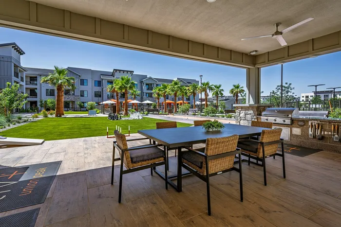 Inviting outdoor seating area with stylish dining set, modern grill, and lush green views framed by palm trees and contemporary apartment architecture.