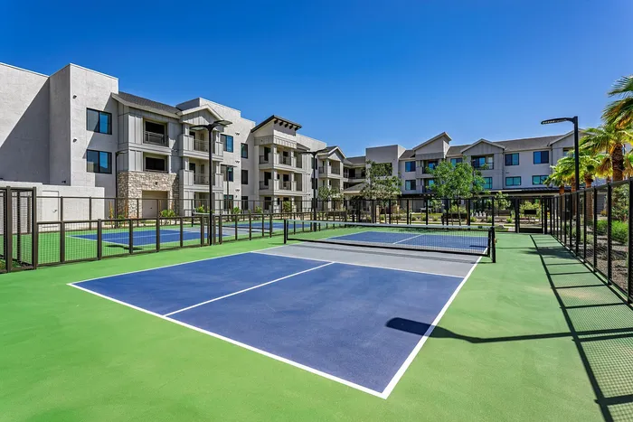 Modern apartment complex with luxurious tennis courts surrounded by lush greenery and clear blue skies.