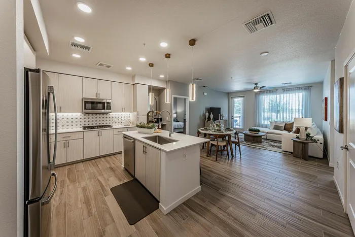 Modern open-plan kitchen and living area featuring elegant wood flooring, sleek cabinetry, and stylish lighting fixtures.