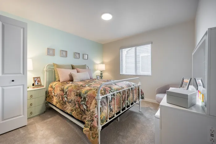 Bright and inviting bedroom featuring a cozy floral-patterned bed, soft lighting, and stylish decor.