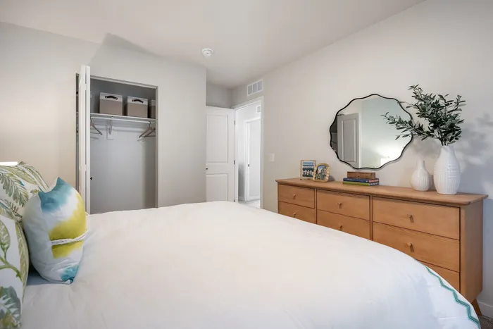 Bright and inviting bedroom with elegant decor, featuring a spacious bed, wooden dresser, and modern mirror for a cozy living experience.