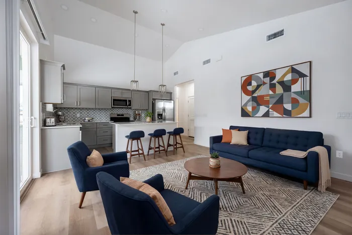 Elegant open-plan living space with a modern kitchen, featuring sleek gray cabinets, a stylish geometric backsplash, and a cozy navy seating area.
