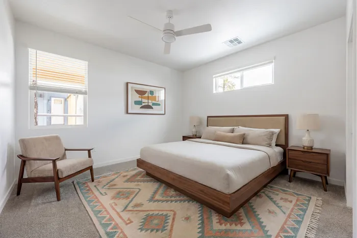 Bright and modern bedroom showcasing a minimalist design with a cozy queen bed, elegant wooden furniture, and soft carpeting.