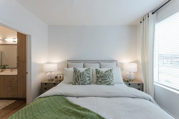 Bright and elegant bedroom with modern design featuring a cozy bed, leafy patterned cushions, and soft natural lighting. Luxurious comfort meets stylish d&eacute;cor.