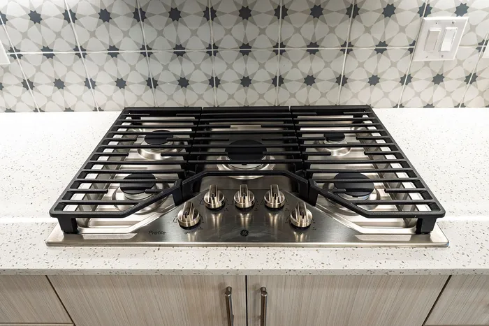 Sleek kitchen with modern gas cooktop on a sparkling quartz countertop, enhanced by a stylish geometric tile backsplash.