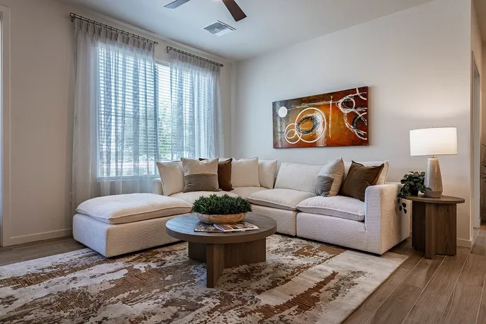 Inviting living room with plush beige sectional sofa, modern abstract art, and natural light streaming through large windows.