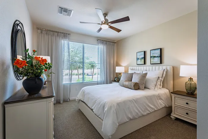 Inviting, sunlit bedroom with elegant decor, featuring a cozy bed, stylish dresser, and vibrant floral arrangement.