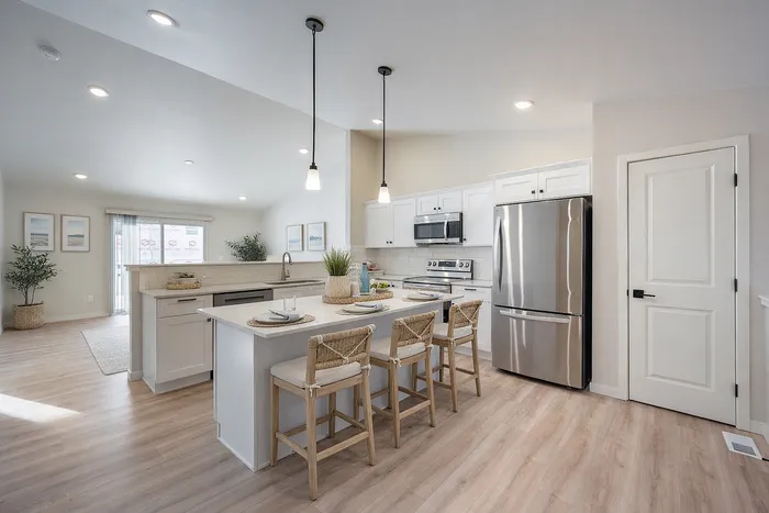 Bright and modern kitchen with sleek white cabinetry, stainless steel appliances, and a stylish island with seating, accented by pendant lighting.
