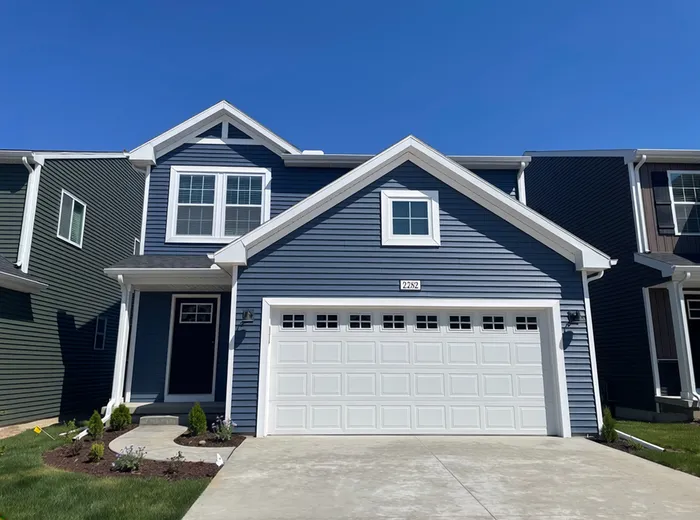 Charming two-story blue house with white accents, featuring a welcoming front porch and a spacious two-car garage.