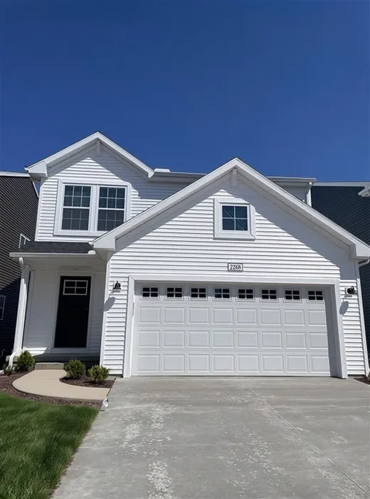 Charming modern home with sleek white exterior, featuring a two-car garage and inviting front porch under a clear blue sky.