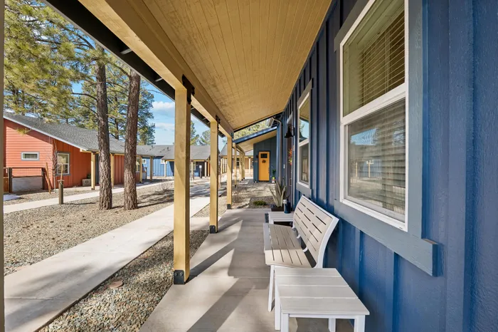 Charming outdoor walkway with rustic wooden pillars and cozy seating on a sunlit patio in a picturesque community setting.