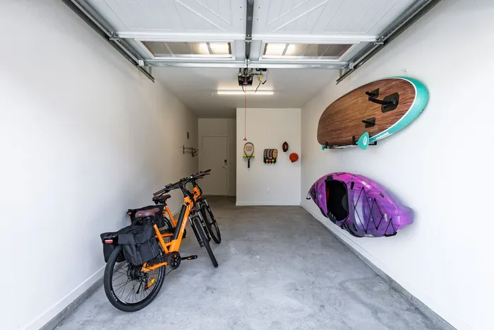 Bright and spacious garage featuring neatly stored bicycles, a hanging paddleboard, and kayak, perfect for adventure enthusiasts.