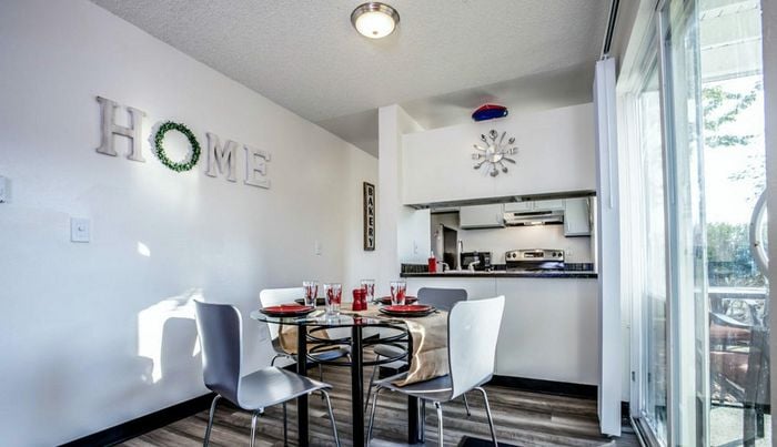 Bright dining area with a glass table set for four, adjacent to a modern kitchen with stainless steel appliances.
