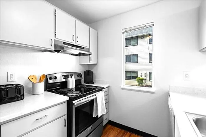 Bright and modern kitchen with sleek white cabinetry, stainless steel appliances, and natural light from a window.
