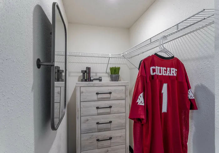 Chic closet area with a stylish mirror, drawer chest, and hanging sports jersey.