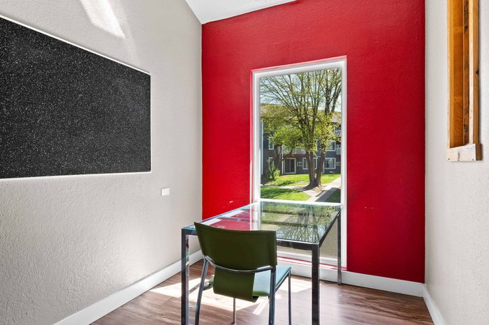 Bright, modern study area with a glass-topped desk against a striking red accent wall, offering a picturesque view of a lush courtyard through a large window.
