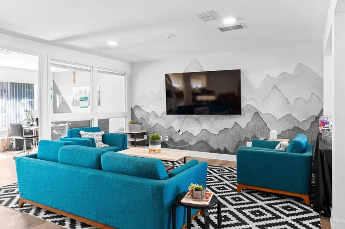 Modern living room with vibrant turquoise sofas, geometric black and white rug, and large wall-mounted TV, creating a stylish and inviting atmosphere.