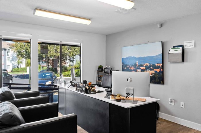 Modern office space with sleek black furniture, large windows offering natural light, and a scenic cityscape painting enhancing the ambiance.
