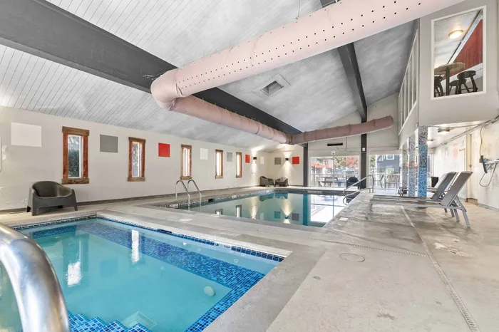 Luxurious indoor swimming pool with modern lounge chairs and vibrant wall art, perfect for relaxation and leisure.