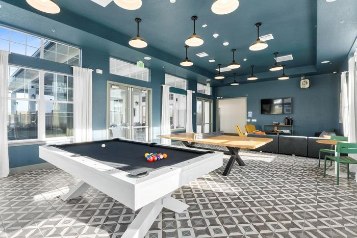 Bright recreation room with a pool table, ping pong, stylish seating, and geometric tile floor.