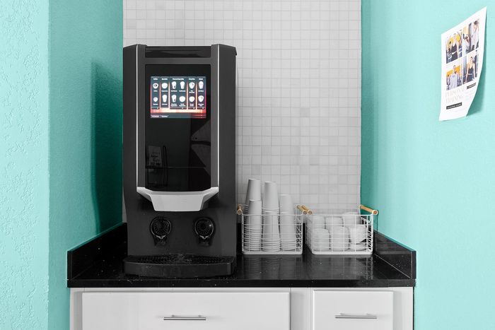Modern coffee machine setup on a sleek black countertop with neatly arranged cups and an inviting teal wall.