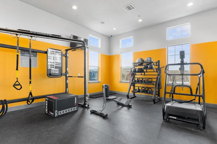 Contemporary fitness room with TRX equipment, kettlebells, and bright yellow walls.