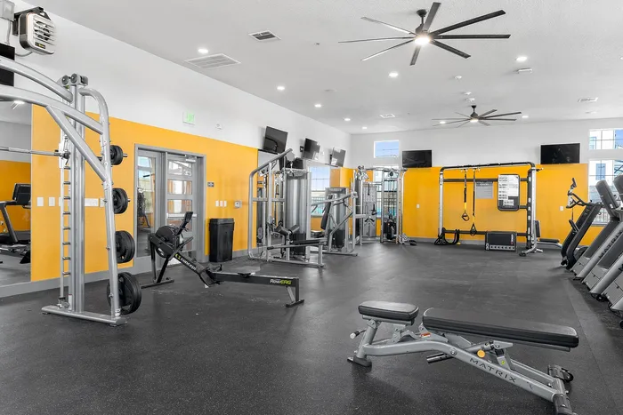 Modern gym with various fitness equipment, yellow walls, and ample open space.