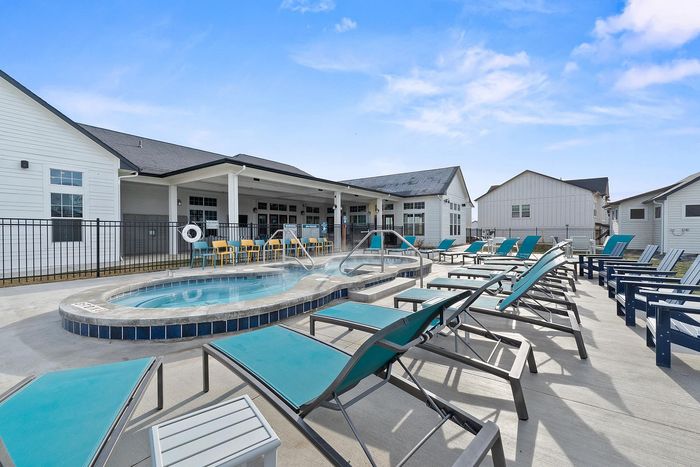 Scenic pool area with sun loungers and a modern clubhouse under a clear blue sky.