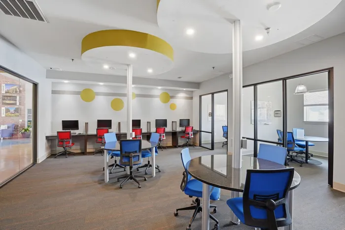 Modern shared workspace with vibrant seating, computer stations, and glass-enclosed meeting rooms, designed for productivity and collaboration.