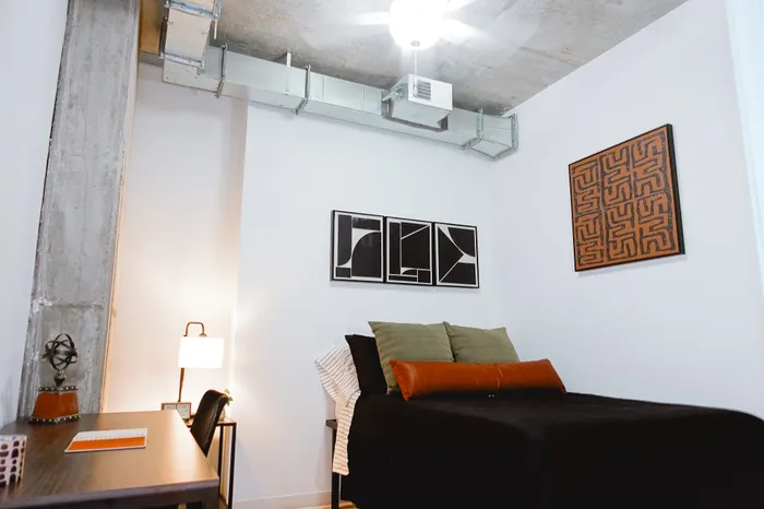 Cozy bedroom with modern industrial vibes, featuring chic artwork, a stylish desk area, and a comfortable bed, perfect for urban living.