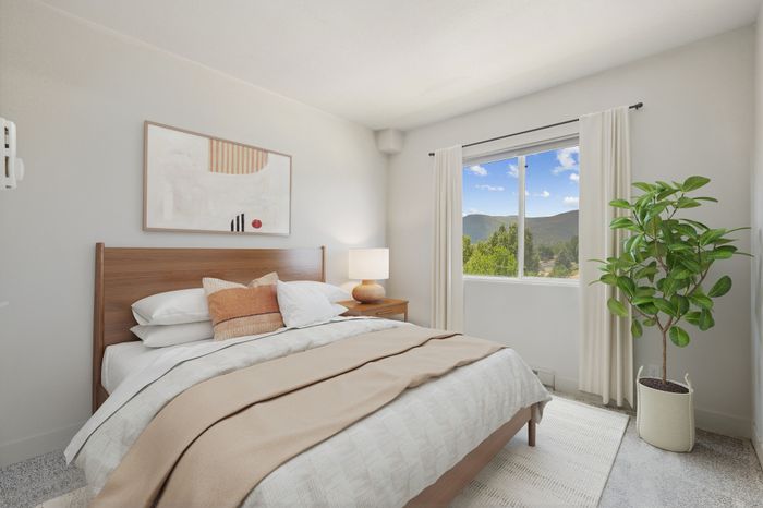 Bright and cozy bedroom with natural light, featuring a modern wooden bed, elegant decor, and a scenic window view of lush greenery and mountains.