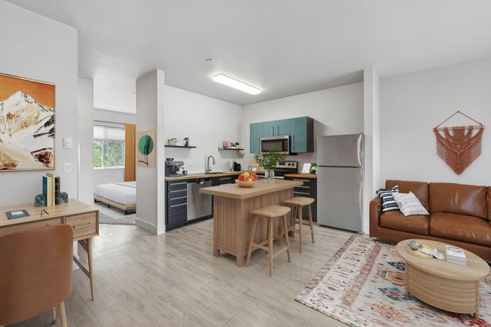 Modern apartment interior featuring an open-plan kitchen with sleek cabinetry, cozy living area with a stylish leather sofa, and a practical workspace with a chic desk.