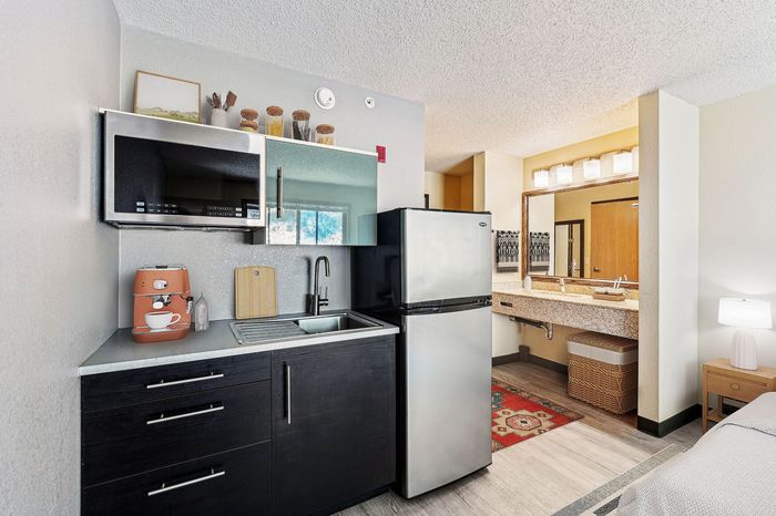 Modern apartment kitchenette with sleek metal appliances, elegant sink area, and vibrant decorative accents, adjacent to a cozy, well-lit living space.