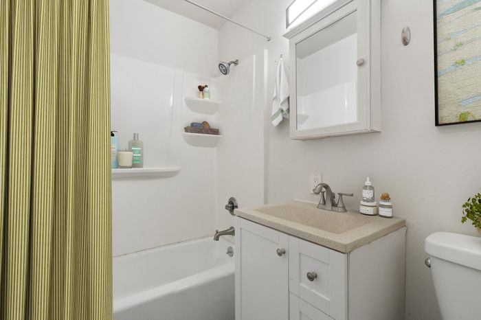 Modern and elegantly designed bathroom featuring sleek fixtures, a pristine bathtub with a striped shower curtain, and ample storage space.