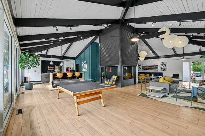 Chic communal lounge featuring a modern table tennis setup, stylish seating area, and sleek bar section under vaulted ceilings with contemporary lighting.