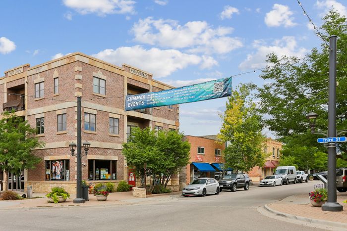 Charming corner building with classic brickwork and vibrant storefronts, set in a sunny, tree-lined street perfect for urban strolls.