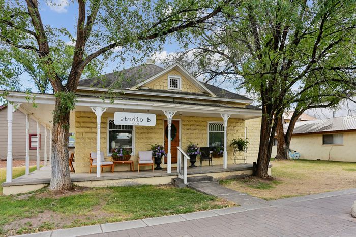 Charming stone bungalow with inviting front porch, lush garden accents, and cozy seating in a tranquil setting.