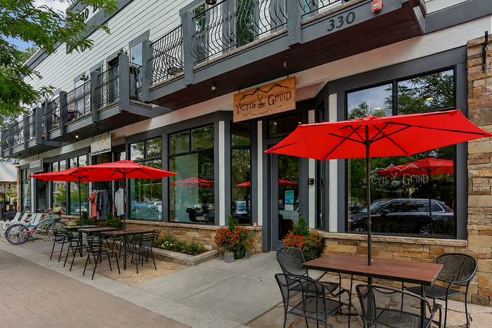 Charming caf&eacute; exterior with red umbrellas and cozy outdoor seating, perfect for enjoying a sunny day.